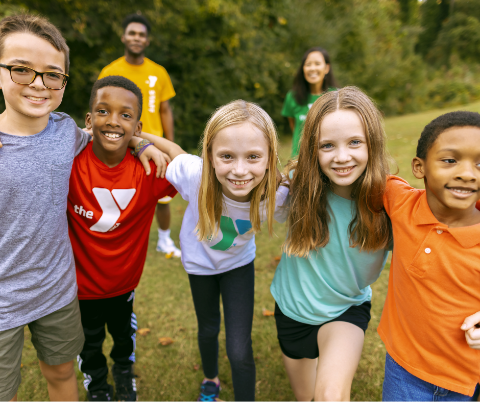 group of kids gathered on a field with two ymca camp counselors