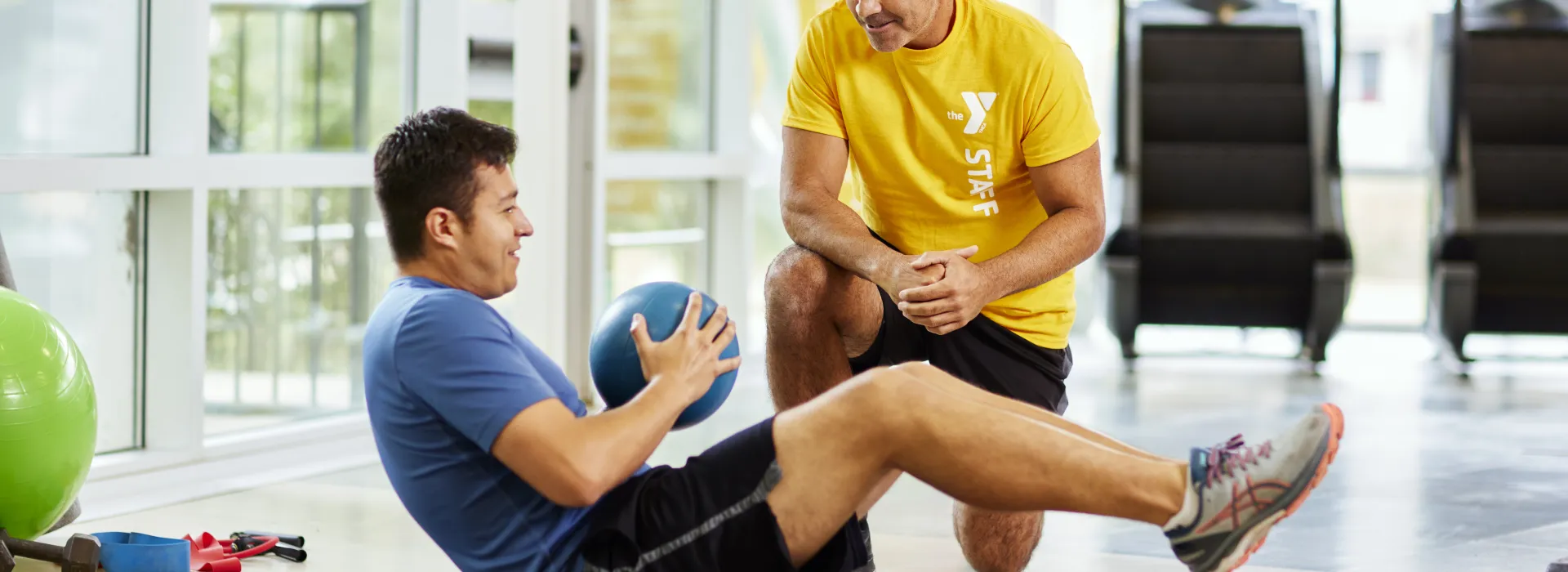 Personal trainer kneeling beside a member performing crunches with medicine ball